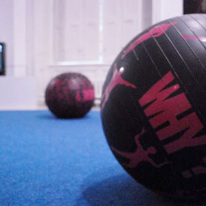 Gymballs are set on a blue carpet, texts and silhouettes are drawn on them.
